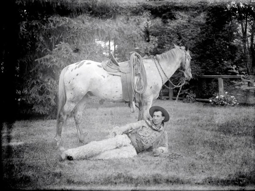 A man identified as Martin Schmitt is lying in the grass in front of an appaloosa horse, The Electric Studio/O.G. Allen photographs, ca. 1911-1913