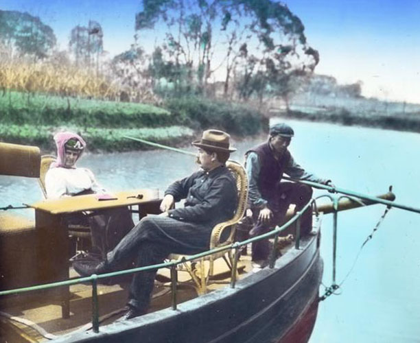 Two individuals identified as Gertrude Bass Warner and Murray Warner sit on their houseboat Illinois with a guide., Gertrude Bass Warner (1863-1951) photographs