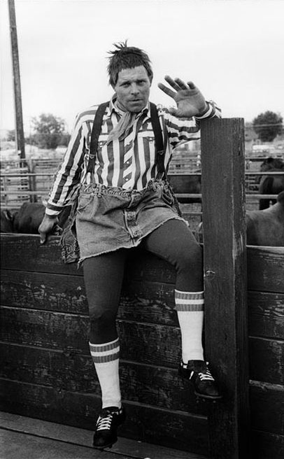 A rodeo clown sits on a fence with a hand raised towards the camera, Grayson Mathews (1948-2007) photographs, 1970s-1990s