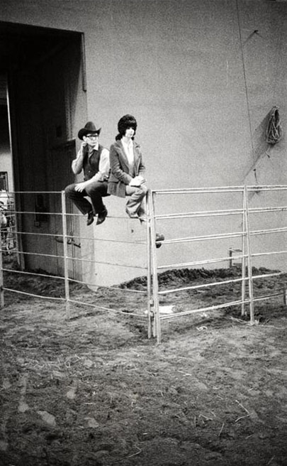 A man and a woman sit on top of metal pen fencing, Grayson Mathews (1948-2007) photographs, 1970s-1990s
