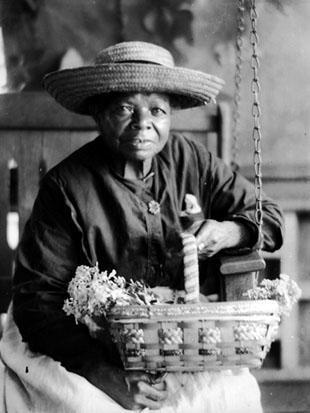 African-American woman in big straw hat, holding basket of flowers