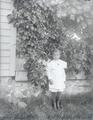 Young boy standing next to house and shrub