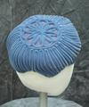 Cap of wide, powder blue chenille cord wound around the head form with a flower design at the crown