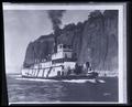 The 'River Queen' sternwheeler on river, tall rock cliffs in background; 2 covered wagons on deck.