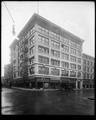 Beck Building at corner of Broadway and Oak, Portland. Stores at street level, telephone company on corner. Autos and motorcycle parked at curb.