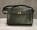 Handbag of black faux leather with gold twist closure at center-front flap