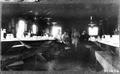 Smith Powers logging camp.  Interior view of dining area, long trestle tables, hanging oil lamps. Dishes on tables. 2 men, 2 women.