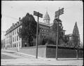 Buildings of St. Mary's Academy, Portland, on hill supported by stone wall. Tower of main building framed by two power poles in foreground.