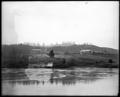 Distant view of St. Mary's Academy (Marylhurst) campus. Two buildings with power plant between. Small building along river in foreground.