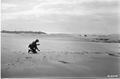 Man kneeling on dunes, examining object in hand