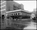 Vacant building on site of Ritz Hotel, N. W. Park and Morrison, Portland. Theatre posters in store windows, man with umbrella on foreground corner.