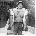 Boy standing in boat holding 2 large fish