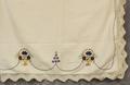 Tablecloth of white cotton with machine embroidered motifs of baskets of flowers and flower motifs in yellow, red, and blue