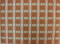 Textile of clay red and greenish grey cotton plaid with vertical stripes of red and black raised woven lines trimming the plaid pattern