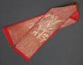 Sash of red crepe with fern or palm trees at each end and background of curved lines of couched gold metallic threads
