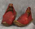 Shoes of red textured leather with brown leather soles that extend beyond the shoe