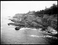 Distant view of large house on cliff, Shore Acres, OR. Ocean and rock formations in foreground.