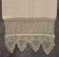 Towel of white linen bordered at both ends with drawn work in a wheat or vine-like design and hand-knotted lace ending in fringe