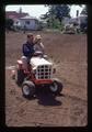 Man and girl riding small tractor, 1975