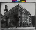 Wadhams & Kerr Bros. Wholesale Grocers on Hoyt at 4th, Portland. Groceries on carts along street, houses next to building, water tank on roof. (recto)