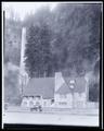 Lodge at Multnomah Falls. Stone building with falls in background, auto parked on highway in foreground.