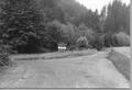 View of fork in road with sign in middle. "Siuslaw National Forest Boating Site Launching" Forest in background, sign, portal at launching.