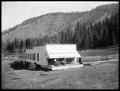 Rondowa Hotel and post office at Rondowa, OR. Isolated building with people on awning-covered porch. Hillside in background.