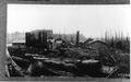 Smith Powers logging camp.  Several buildings with logs in foreground. Snags tree stumps in background