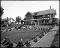 Henry home with lawn and garden in foreground. Gravel sidewalk along garden in foreground. Smaller house in background.