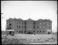 Full view of Hotel High Line, Granger, WA. Staff standing in front of hotel, dirt street in foreground.