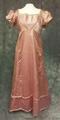 Gown of pink silk satin with lace trim casing a thin black ribbon on bodice