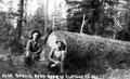 Two men sitting on the ground in front of a felled log