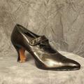 Shoe of black patent leather with pointed toe and button strap over instep