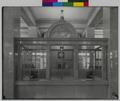 Interior detail, two tellers' cages in US National Bank, Portland. Bars and glass windows on counter, wall clock above windows. (recto)