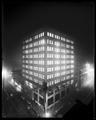 Night photo of Corbett Building, Portland. Elevated view with lights on in all windows. Power lines below in foreground.