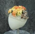 Hat composed of a bouquet of yellow and orange synthetic flowers with green leaves and stems tied with a wide ribbon bow of taupe velour