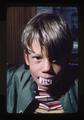 Boy posing with novelty fanged teeth, 1975