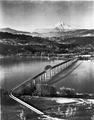 An interstate toll bridge between Hood River, OR and White Salmon, WA. Shows approaches from WA side with Mt. Hood, partial view of Hood River, and panoramic view of Hood River County.