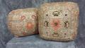 Armrest cushion of woven beige/taupe silk ground with cool grey, lilac, bright red, brown, peach, ecru, and black silk embroidery in floral and lotus motif set in a central square with a blocked outer square