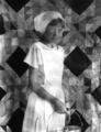 Girl with cap, in front of quilt, holding kettle