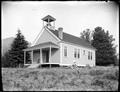 One room school with bell tower, near Myrtle Point, OR. Woodpile beside school, trees in background.