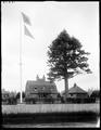 Life Saving Station at Flavel, OR. Wood buildings next to tall tree in background, fence in foreground.