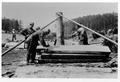 CCC workers sawing logs to make half log table top. Log propped up to saw thru center.