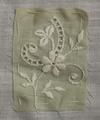 Textile sample of pale green woven cotton with white embroidered floral spray with leafy vines