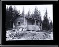 Log cabin with front porch, in rural setting. Couple sitting on porch.