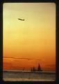 Airplane taking off at sunset, sailboats on the water below, 1975