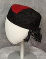 Hat of pillbox-shape of red felt and black solid embroidery around the sides and half of the crown
