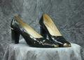 Pumps of black patent leather with square toe tipped in a bar of gold metal
