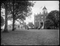 Building with clock tower on campus of McMinnville College. People on steps of building. Larger building behind trees in background.