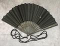 Folding fan of carved black wood sticks mounted with sheer black silk embellished with tiny black paillettes